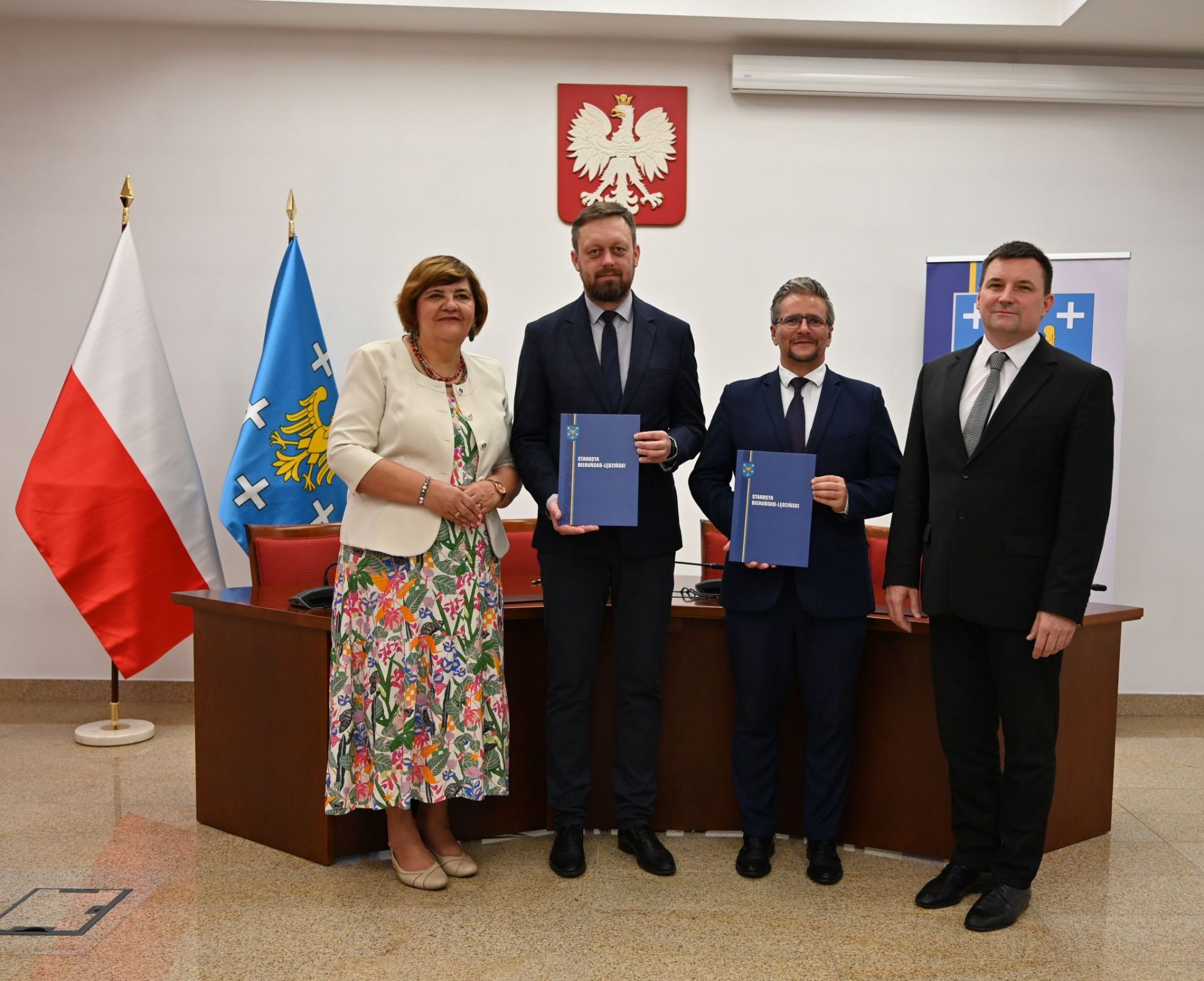 Zdjęcie czterech osób dwie stojące w środku trzymają dokumenty.